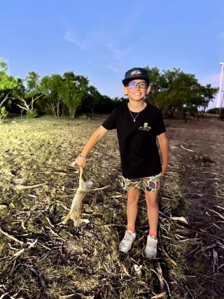 A young hunter smiles while holding a rabbit taken at BarBell Ranch in Sweetwater, TX.