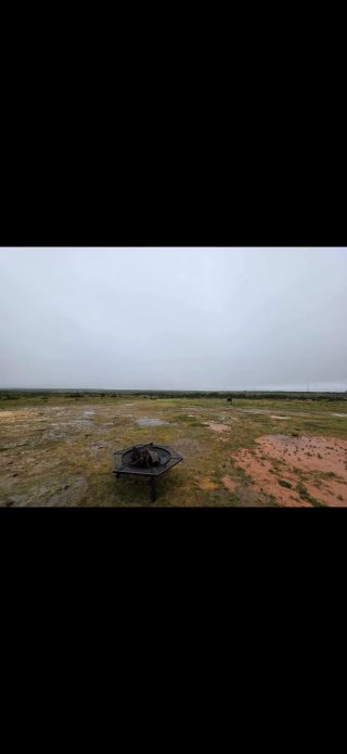 Rustic fire pit with wood ready to burn, with distant Texas landscape under a heavy sky at BarBell Ranch.