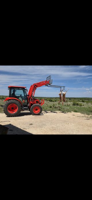 A rancher operates a tractor with two whitetail deer hanging in the loader lift at BarBell Ranch.