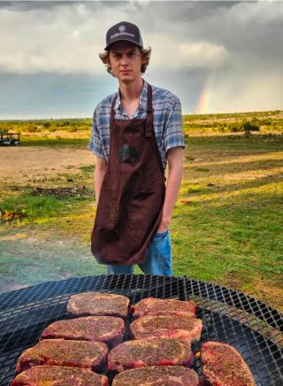 A chef at BarBell Ranch grill steaks while a rainbow accents the West Texas sky.