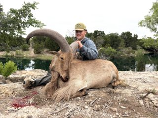 A hunter with his aoudad ram from BarBell Ranch in Sweetwater, TX beside a waterhole.