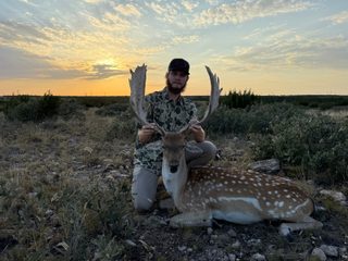 Hunter with a Fallow Buck taken at BarBell Ranch in Sweetwater, TX, beneath a vivid sunset sky.